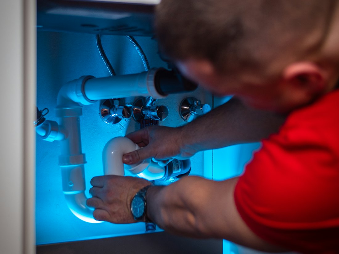 Plombier raccordant un siphon sous un évier